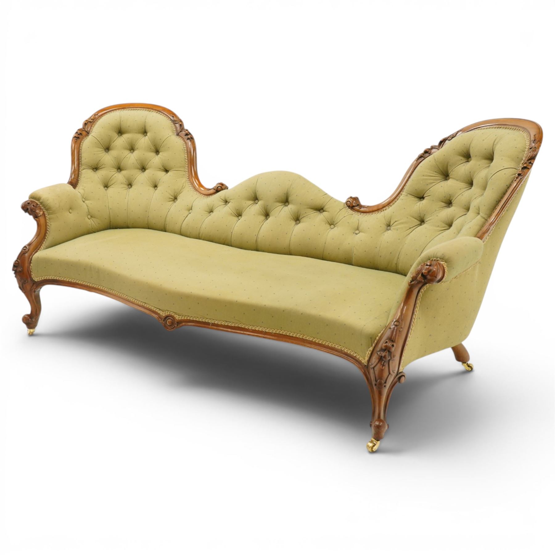 Victorian mahogany framed double ended chaise longue, serpentine button upholstered back with raised scrolled ends, padded arms and stuff-over seat upholstered in green fabric, carved showframe with foliate terminals and scroll supports, on short cabriole legs with brass castors