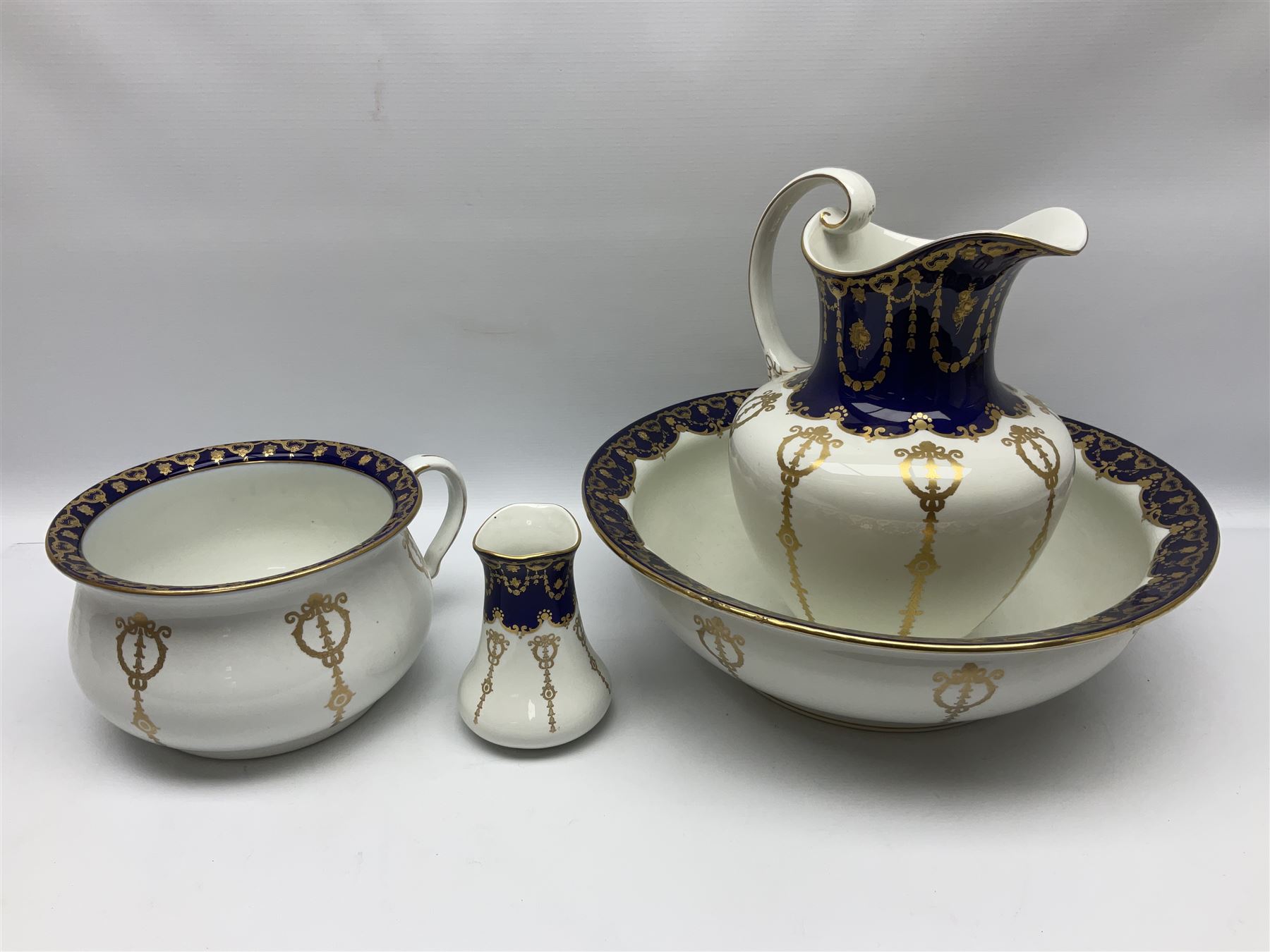 Early 20th century Bishop and Stonier four piece toilet set, comprising washbowl, wash jug, toothbrush pot, and chamber pot, each  decorated with deep blue band and husk swags and festoons in gilt, with printed Caduceus Bisto marks beneath and printed retailers mark 'Manufactured for Harrods Limited London', wash bowl D43cm, wash jug H31.5cm