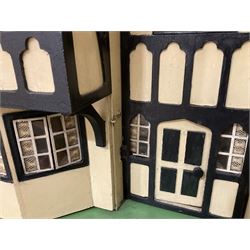 Large Tri-ang No.93 doll`s house in the 'Stockbroker's Range' c1935; two-storey double-fronted Tudor design, half timbered gables, two-storey bay windows, cream and mock shrubbery to front, opening metal framed windows with green shutters, red simulated tiled roof with chimney, integral garage with opening doors, front elevation has four hinged doors opening to reveal two bedrooms with fire places, living room, bathroom and kitchen with built in dresser and sink, entrance hall and staircase, side entrance with porch and seat and sun dial over on chimney stack; some wiring for electrical lighting; metal Tri-ang Toys disc verso; comprehensively furnished H66cm L117cm D43cm