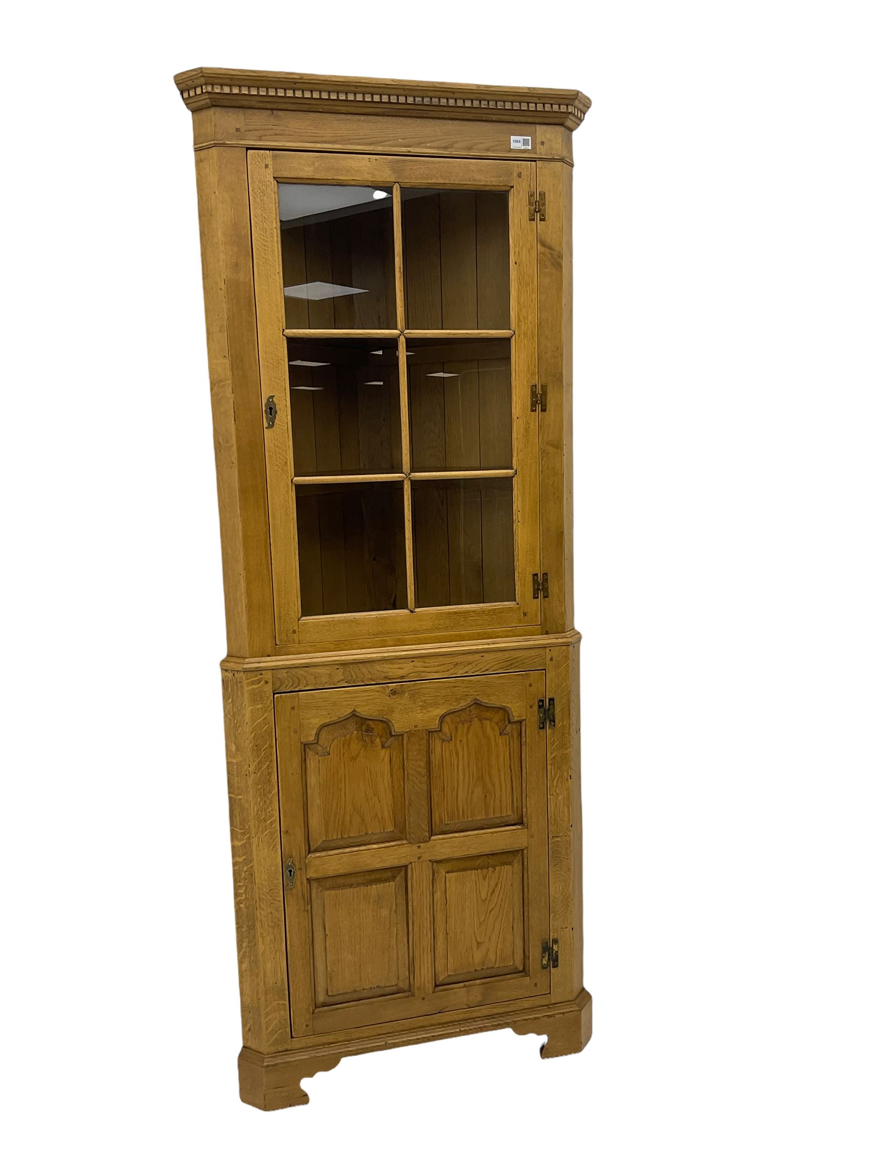Traditional light oak corner cabinet, projecting cornice, dentil frieze, single glazed door above single fielded door