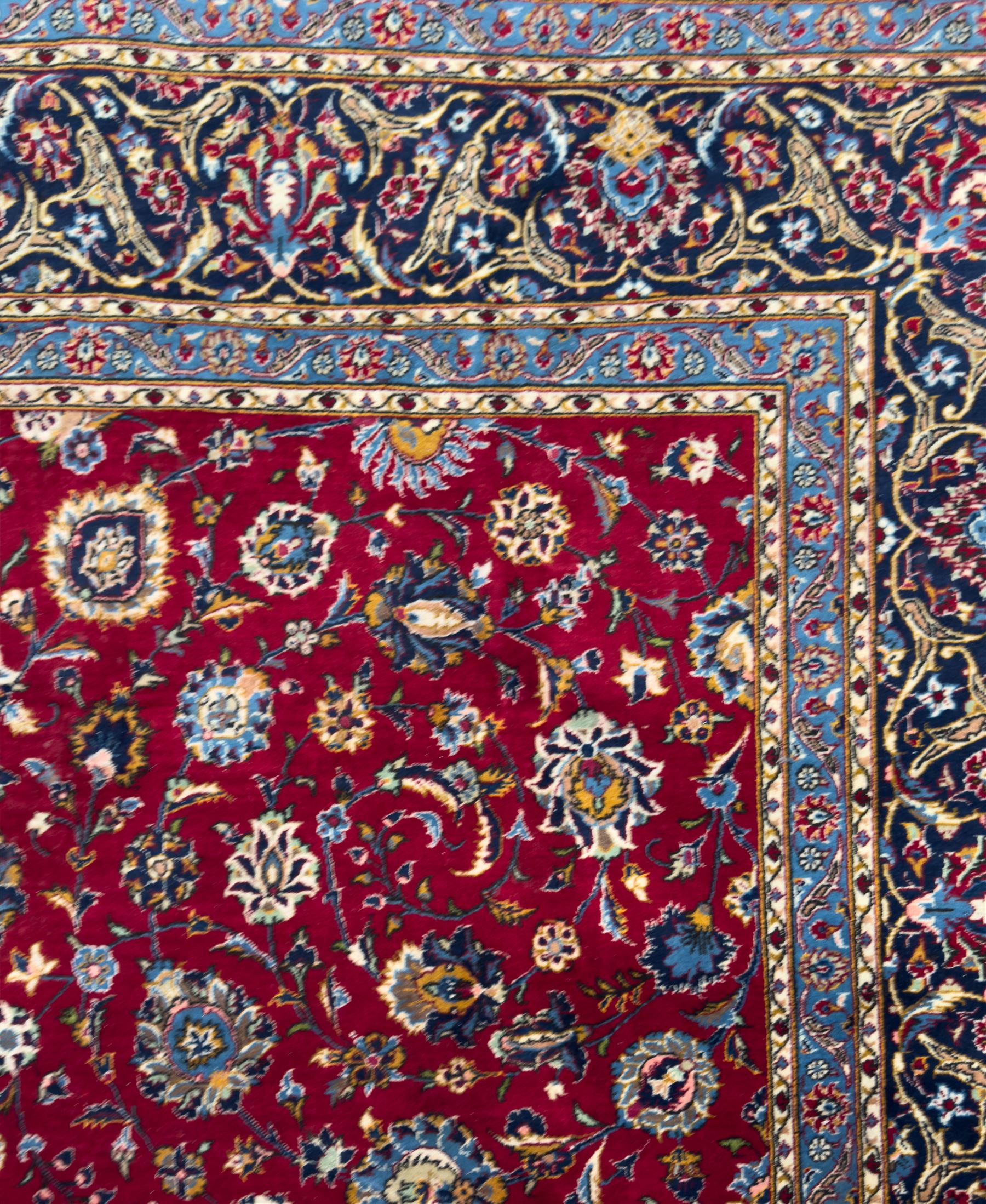 Northeastern Persian Meshed hand-knotted carpet, madder red field with an all-over design of scrolling vines, palmettes, and rosettes, within a dark blue border of palmettes and arabesques 