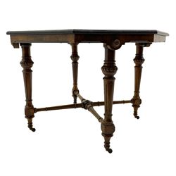 Late Victorian walnut centre table, moulded octagonal top with highly figured quarter veneers, banded in amboyna and ebony with boxwood stringing, the shaped skirt decorated with flower head roundels, on turned and fluted supports joined by fluted x-shaped stretcher rails, on brass and ceramic castors 