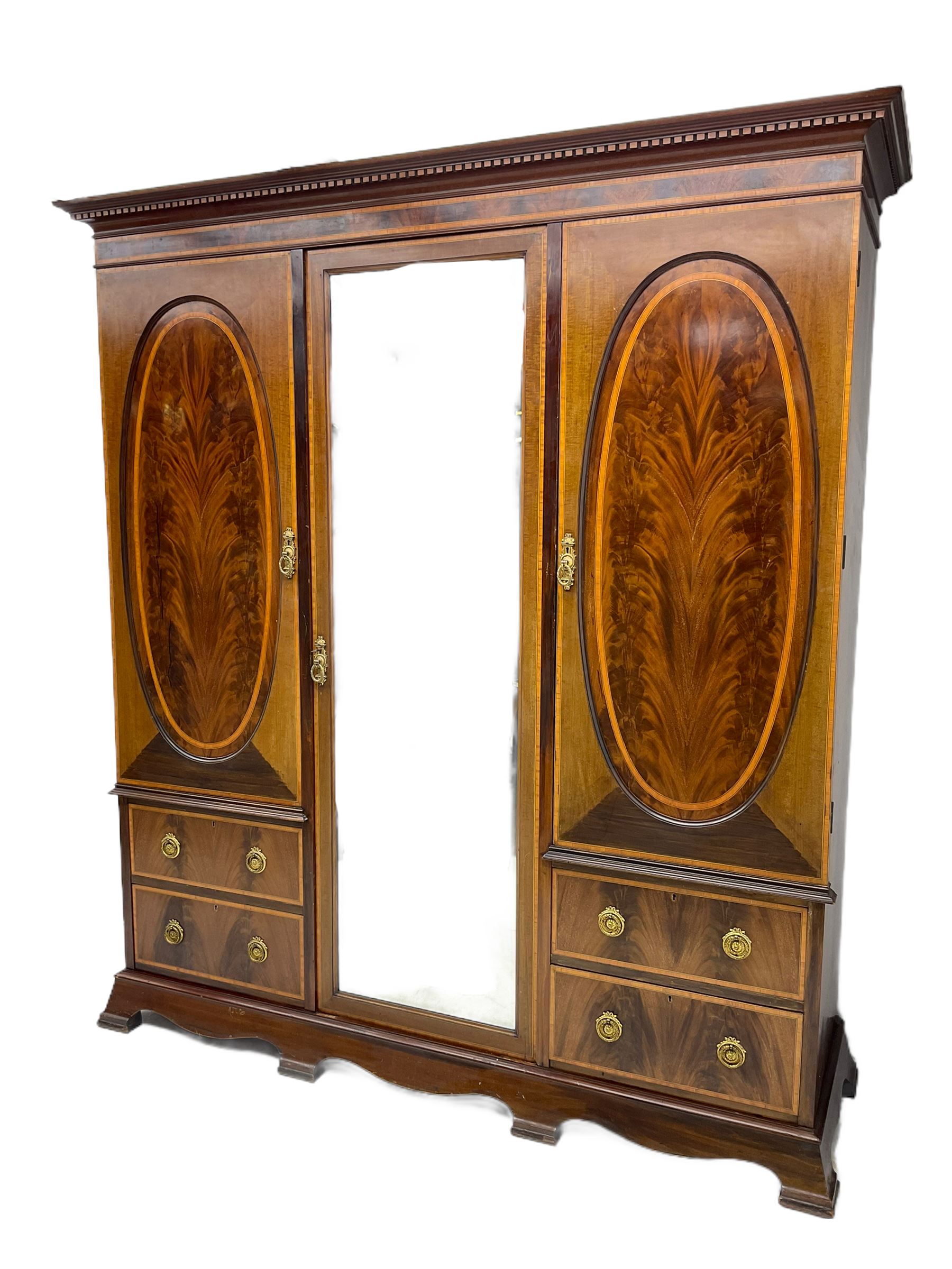 James Shoolbred & Co. London - Edwardian inlaid mahogany triple combination wardrobe, projecting dentil cornice over bevel glazed door, two figured oval panelled doors and four drawers, the central compartment fitted with linen slides and drawers, satinwood banding, on base with shaped apron and bracket feet, with enamel plaque 