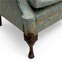 Georgian design carved walnut framed wingback armchair, upholstered in pale blue and gilt floral damask, with shaped loose seat cushion and rolled arms, raised on scallop and cartouche carved front cabriole supports terminating to pad feet