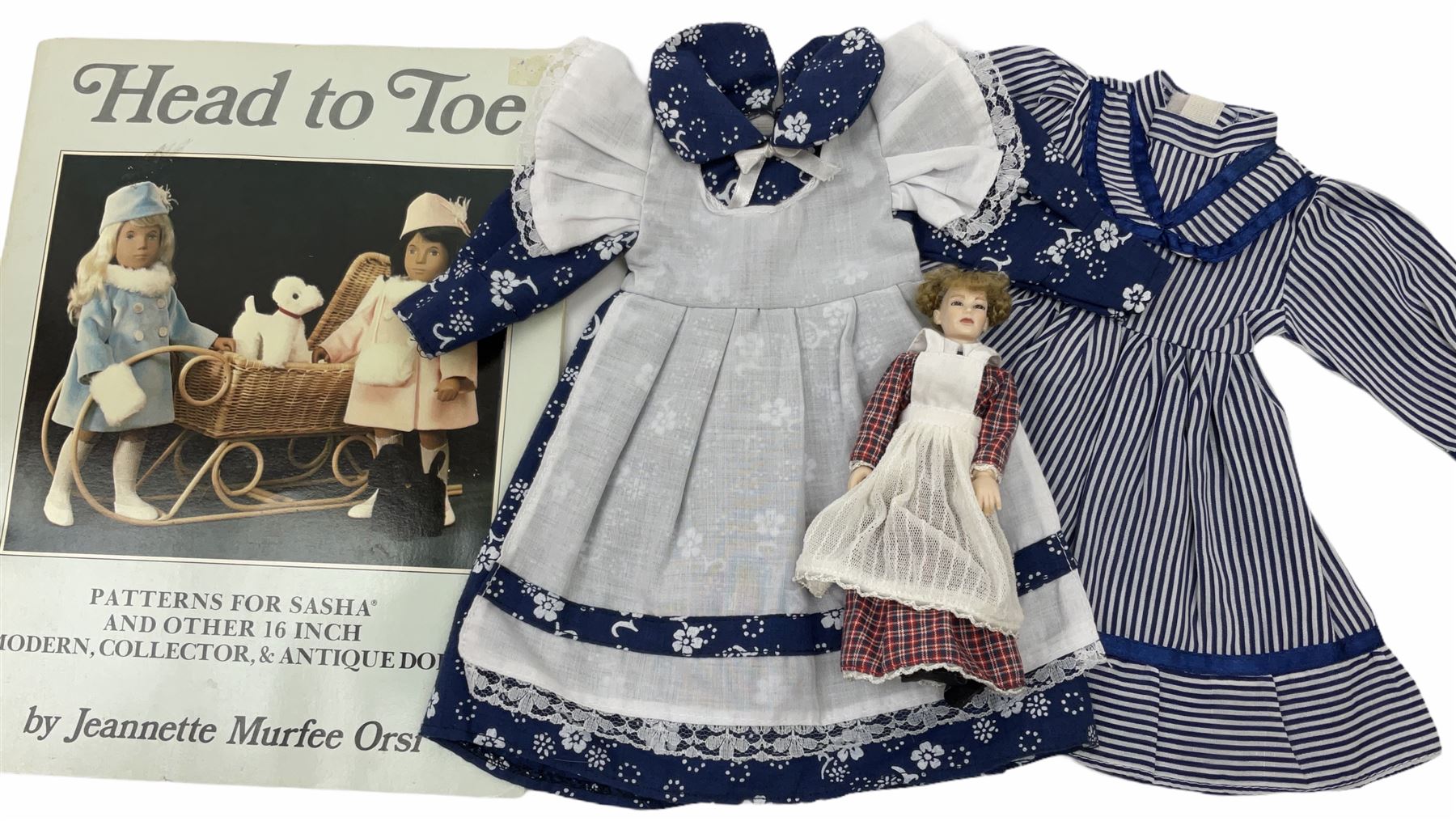 Heidi Ott doll in tartan dress, navy floral dress with white lace and ribbon detailing, striped blue and white dress and a 'Head to Toe' book