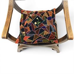 Early 20th century mahogany Savonarola chair, arched leather back with brass studwork, curved open arms with incised geometric decoration, loose patchwork velvet cushion seat, X-frame supports united by circular side rails, on scrolled feet