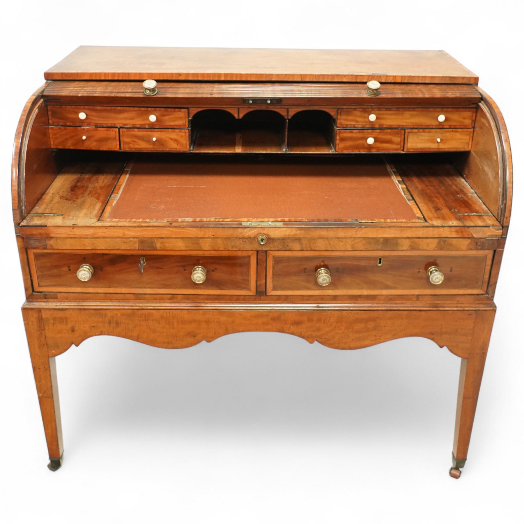 George III mahogany cylinder front writing desk, the hinged tambour enclosing pigeonholes and drawers with bone handles, sliding writing surface with leather inset, three frieze drawers below, on square tapering legs with brass caps and castors