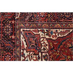 North West Persian Heriz/Ahar hand-knotted carpet, brick red field with a central bold stepped star medallion with pendants, surrounded by angular floral and geometric motifs, ivory spandrels, enclosed by a dark indigo border of stylized rosettes and vine motifs with multiple guard stripes, cotton fringe ends 