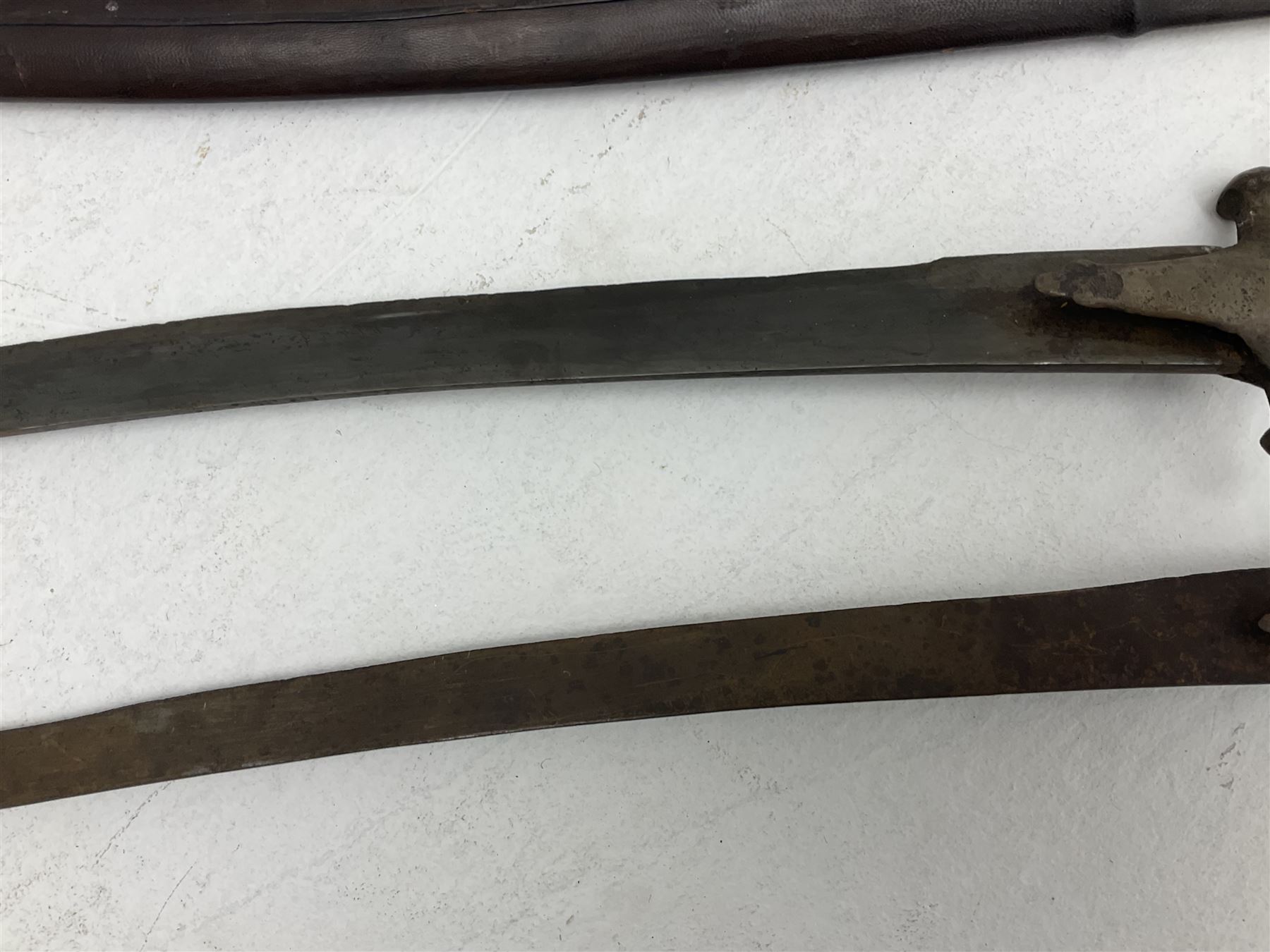 Late 19th/early 20th century Indian Tulwar sword with 81cm plain curving steel blade and iron hilt with extended langets, knucklebow and spiked pommel; in leather covered scabbard L100cm overall; and another Tulwar lacking scabbard in almost relic condition (2)