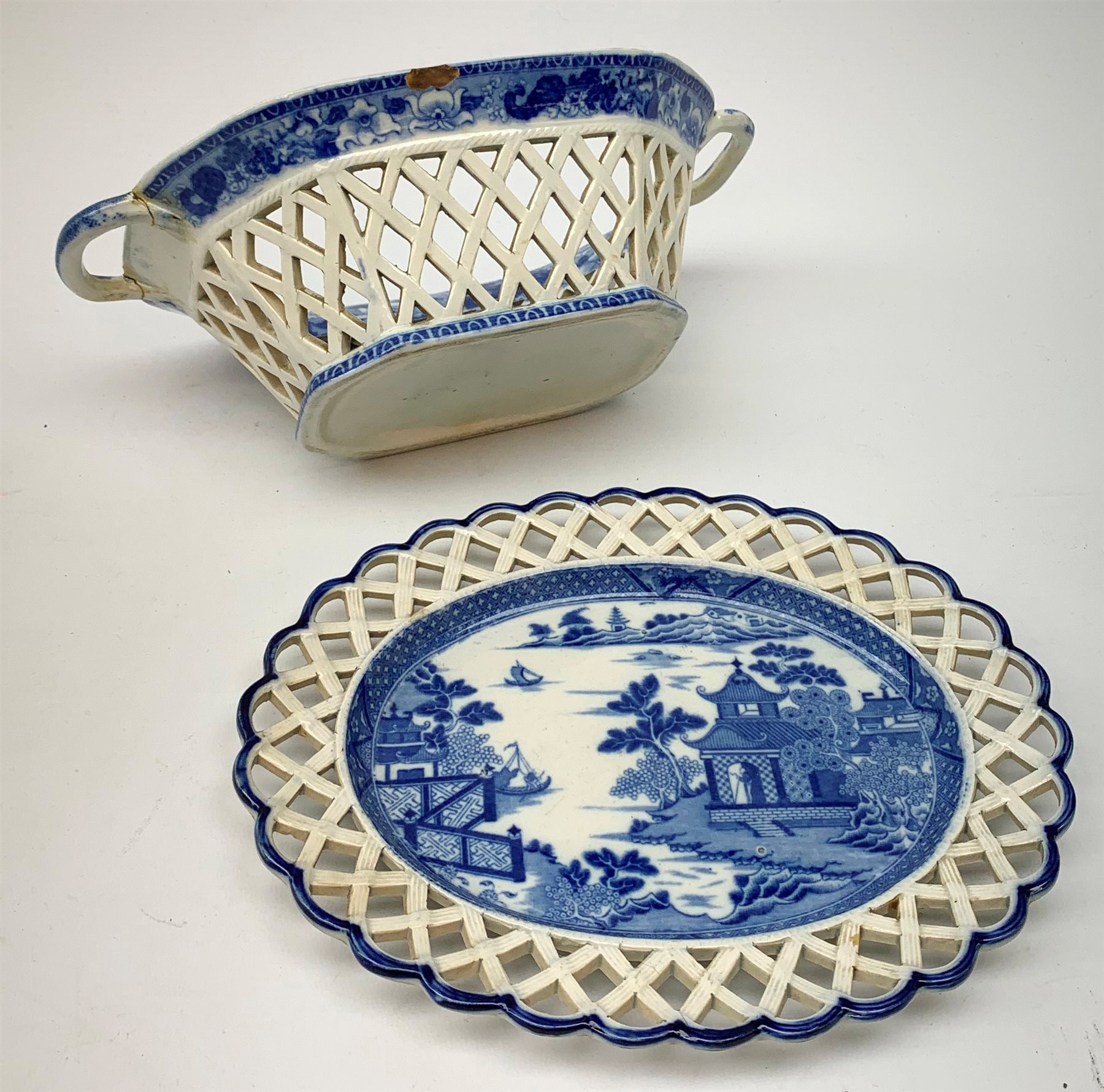 Mid 19th century blue and white transfer printed pearlware reticulated chestnut basket, of oval form with twin handles, decorated to the interior with figures before a classical temple within a garden setting, including handles W26cm, together with a mid 19th century blue and white transfer printed pearlware stand with reticulated edge, decorated with a Willow Pattern, L25cm, and a John and William Ridgeway blue and white transfer printed twin handled pierced basket, decorated with a pastoral scene containing figures at work, with printed mark beneath, including handles L25cm