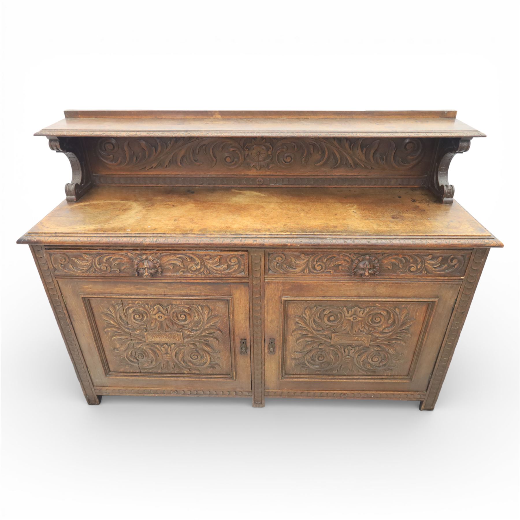 Victorian carved oak sideboard, the rectangular top with raised back carved with foliate scrolls and scroll end supports, upon a base with rectangular top with moulded edge, pair of drawers with conforming carved decoration and mask handles, and pair of carved cupboard doors, upon short stile type feet H101.5cm W183cm D54cm 