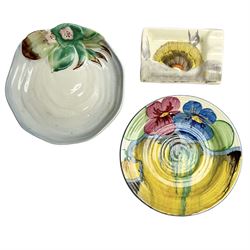 Group of 1930s and later Clarice Cliff small dishes, comprising rectangular ashtray with moulded edge decorated in the Rhodanthe pattern, circular saucer decorated in the Delicia Pansy pattern and further circular dish raised with flowers, predominately in green and pink on merging blue and plain ground, with wavy shaped rim, with Bizarre and Newport stamps beneath, largest D11.5cm