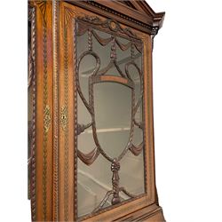 Large and impressive late 19th century Irish mahogany secretaire bookcase, moulded sloped arch dentil pediment decorated with central carved mask surrounded by linen festoons and trailing bellflowers, canted and fluted uprights with carved acanthus leaf upper and lower brackets, enclosed by two astragal glazed doors in the form of trophies with twist ribbon carved mouldings, inlaid with fanned spandrels and trailing leaf painted satinwood band, cylinder roll top inlaid with central fan motif and fanned spandrels, pull-out action revealing stepped fitted interior, central tambour roll cupboard flanked by two Composite pilasters and a combination of drawers and pigeon holes, fitted with three break-front drawers, matched canted and fluted corners with acanthus leaf carvings, on square tapering and fluted spade feet