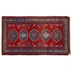 Caucasian Kazak rug, red field decorated with a column of stepped hexagonal medallions in blue, ivory, and crimson, flanked by stylized floral and geometric motifs, enclosed by multiple borders of rosettes and hooked designs 