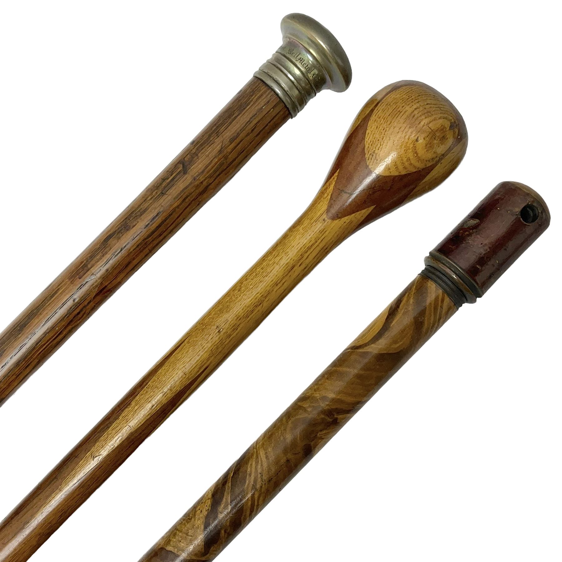 Three early 20th century walking sticks, to include a smoking pipe walking stick, the cane opening to reveal a concealed pipe, and a wooden walking cane, the metal cover with inscription 'bell metal and wood of York Minster, Burnt May 20 1840, and a turned wooden walking stick, with marquetry checkerboard pommel, tallest L90cm