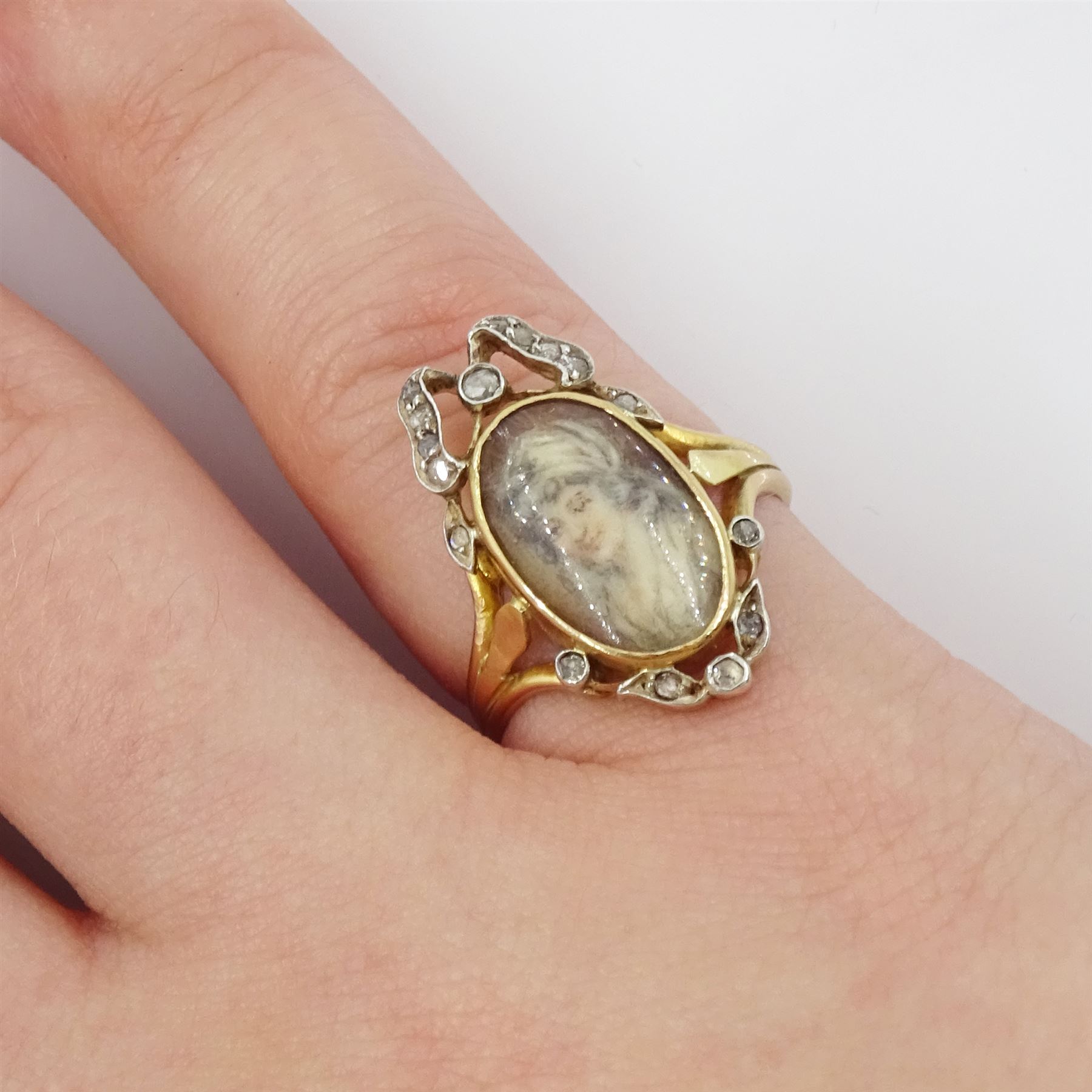19th century gold and silver diamond portrait ring, set with an oval miniature of a woman on ivory, under a glazed panel, with rose cut diamond bow and floral sprigs below, to trifuricated shoulders. This lot has been registered for sale under Section 10 of the APHA Ivory Act