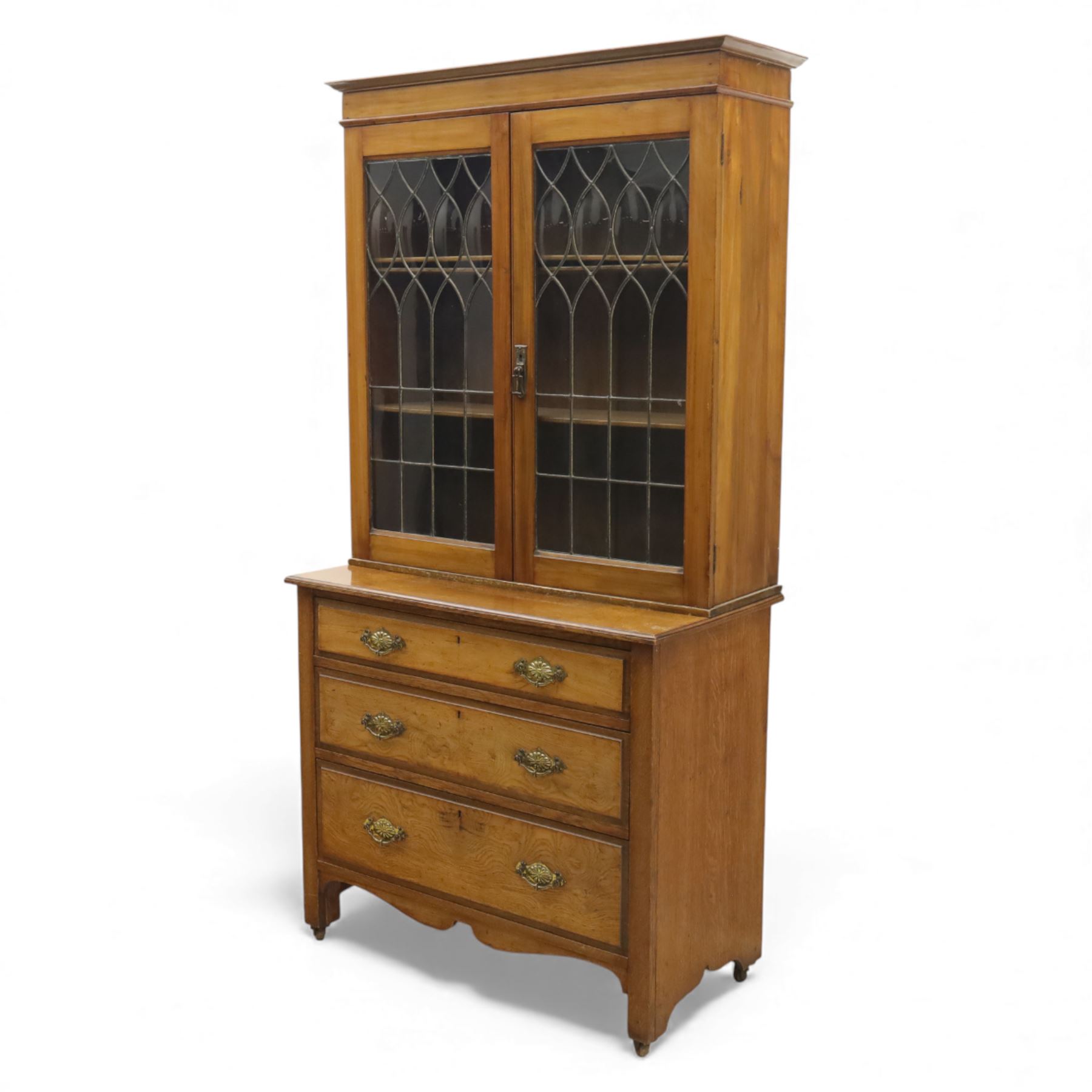 20th century wooden bookcase cabinet, fitted with a pair of leaded glass panel doors opening to adjustable shelves, the base top and front veneered in richly figured walnut, contrasted with solid oak panelled sides and shaped lower frieze, terminating in castors