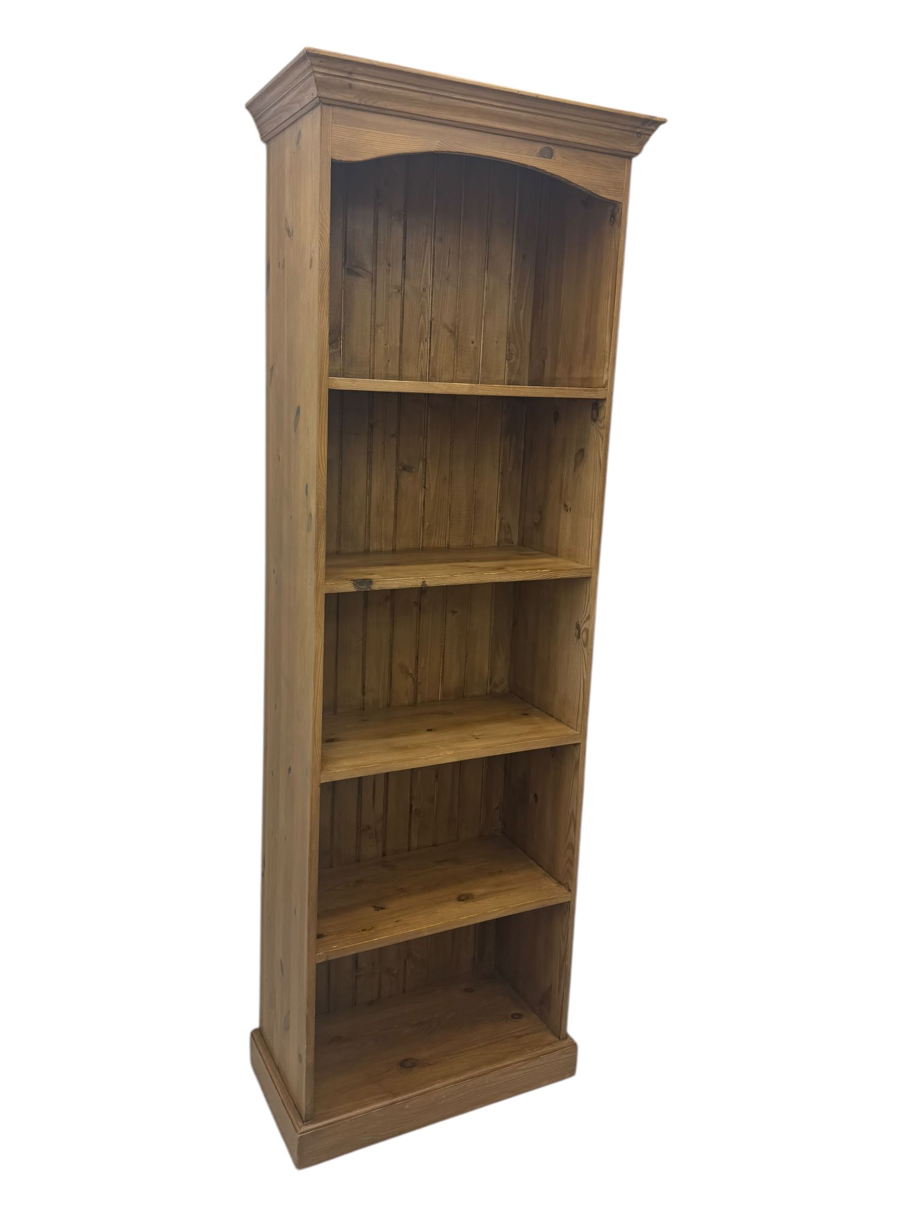 Early 20th century pine bookcase, projecting cornice over arched open shelving area with four fixed shelves, on shaped plinth base