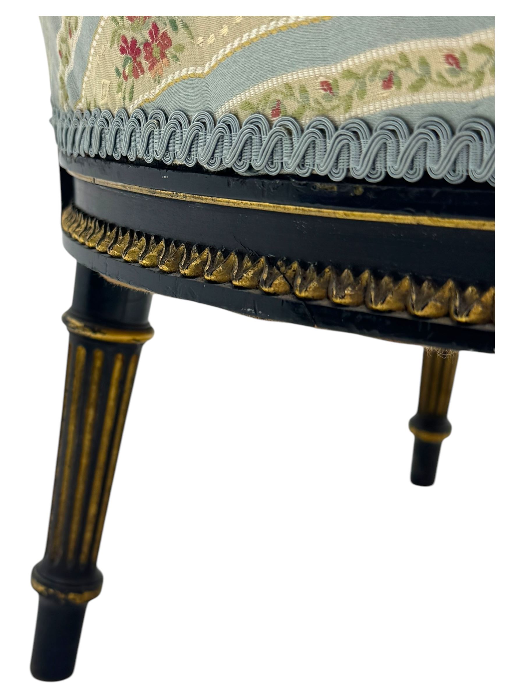 19th century French ebonised low chair, upholstered in floral striped fabric within a moulded frame with gilt line and foliate decoration, the seat of serpentine form, raised on turned fluted legs with toupie feet