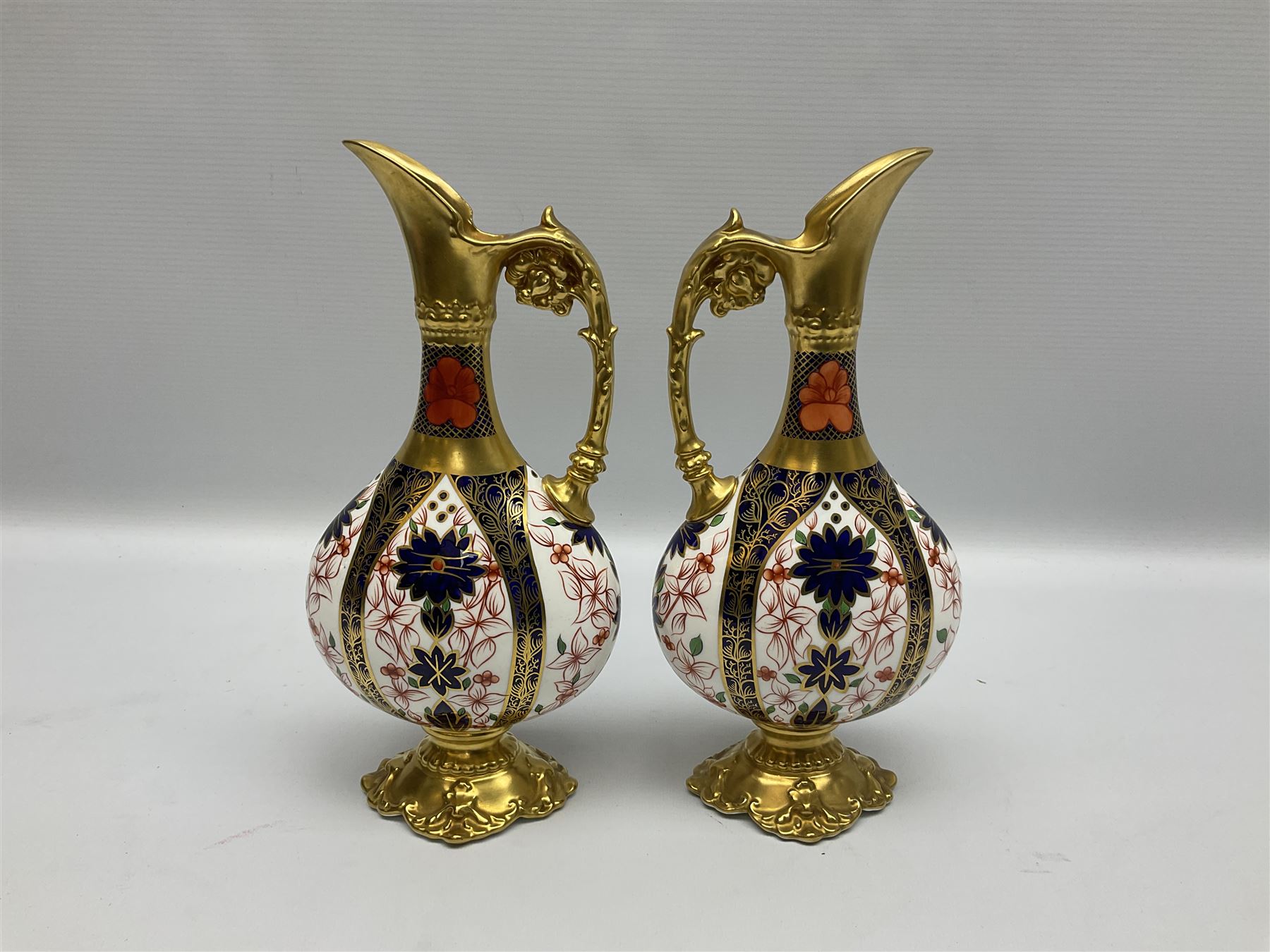 Pair of mid 20th century Royal Crown Derby Imari 1128 pattern Kedleston ewers, each with gilt scroll handle and neck, upon a gilt quatrefoil foot, each with printed marks beneath, H25.5cm