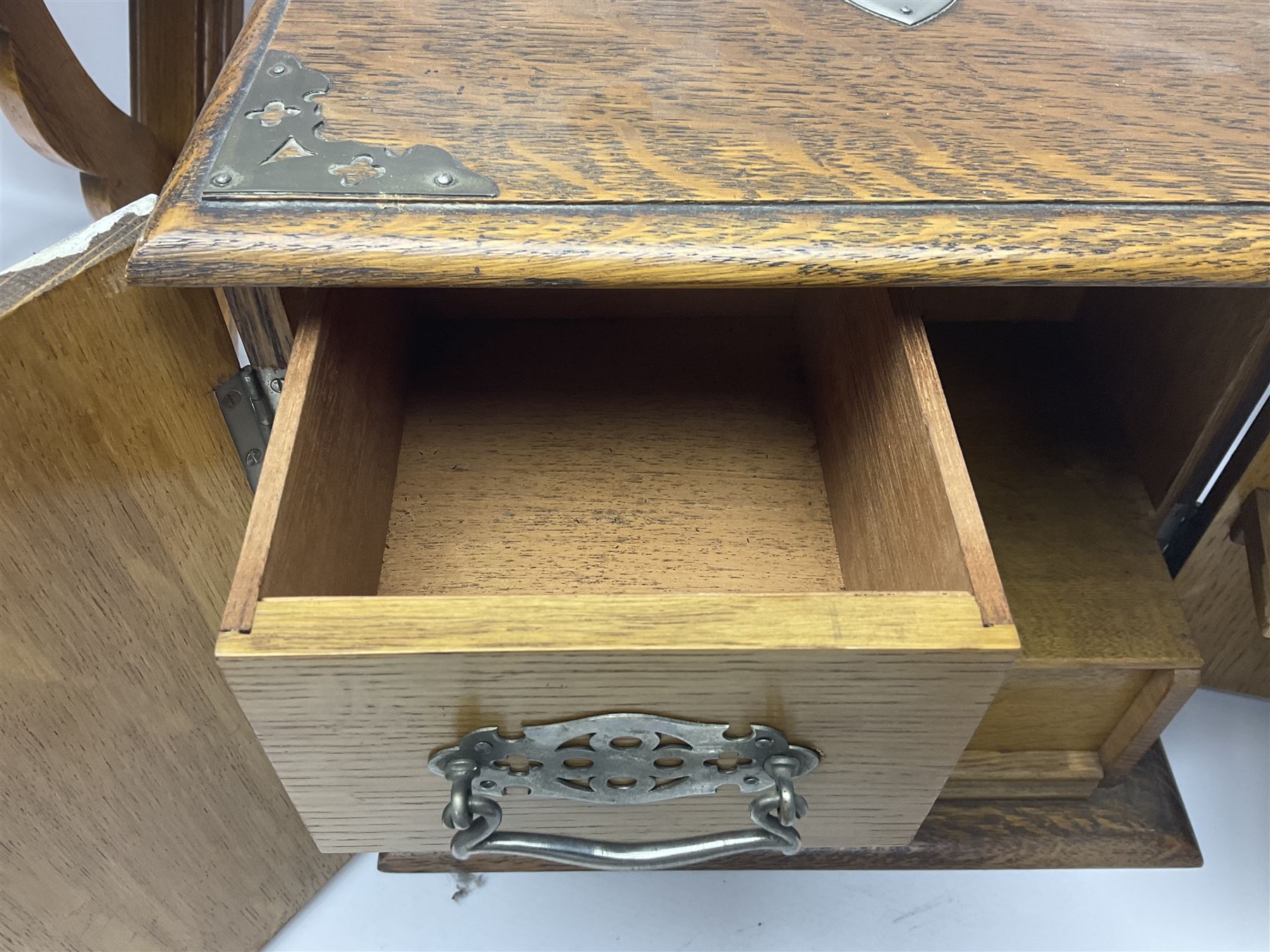 Early 20th century oak smokers cabinet, with brass shield shaped mounts, opening to reveal a compartmentalised interior with three drawers, pipe rack and tobacco jar, together with a small wooden shelf, smokers cabinet H28.5cm