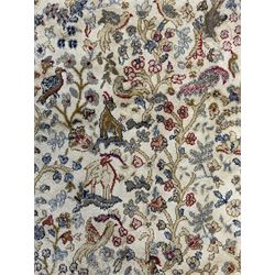 Persian Kerman ivory ground rug, the field adorned with naturalistic depictions of birds, animals and floral designs, framed by a multi-band border in blue and red tones