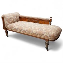 Late Victorian walnut chaise longue, upholstered in geometric patterned fabric, the scroll end and padded back above carved side panel with foliate and roundel motifs, shaped seat rail on turned front supports with ceramic castors
