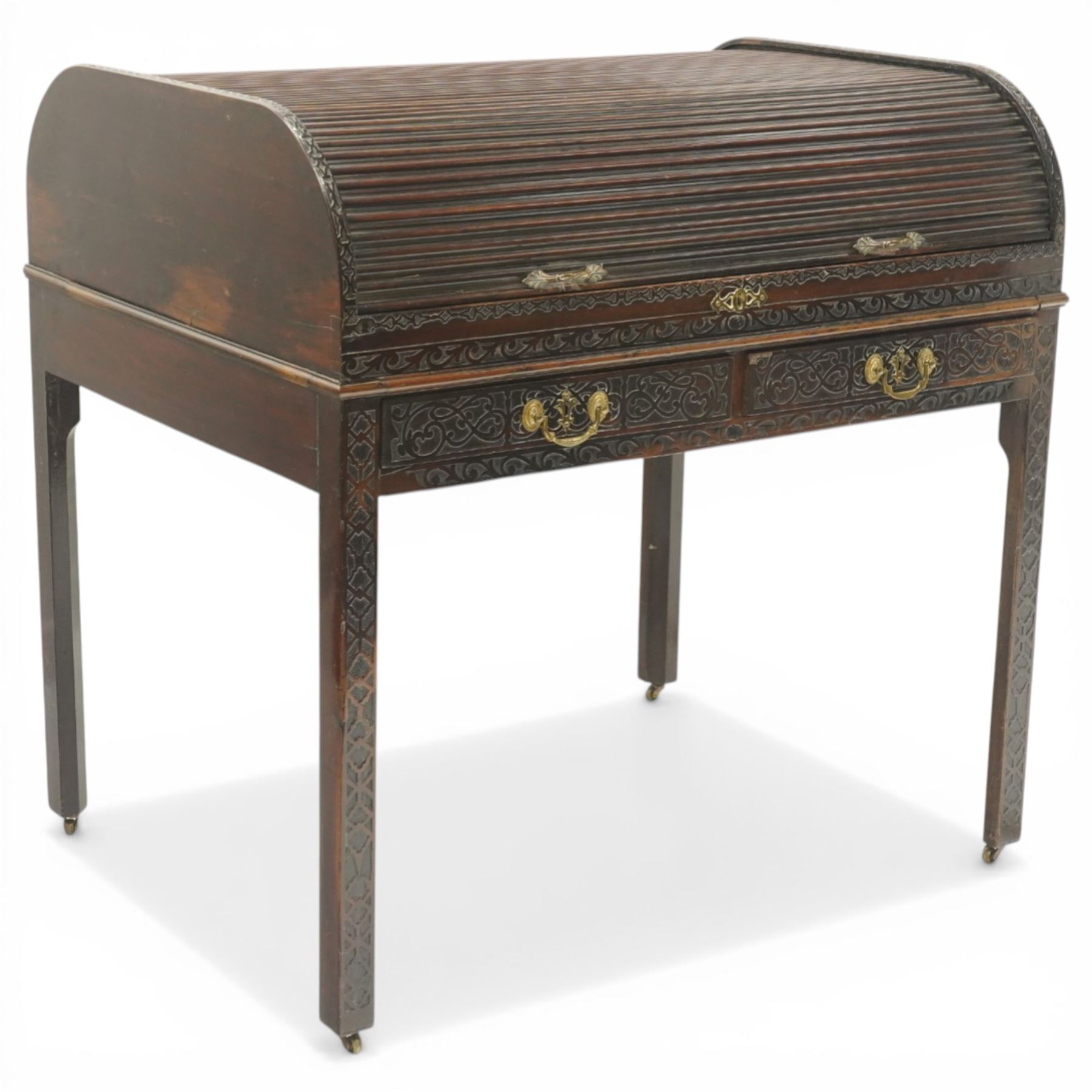 Late 18th century George III mahogany Chippendale design cylindrical roll-top desk carved profusely with geometric and foliate blind-fretwork throughout, the tambour-roll top opening to reveal pigeon holes over an inset red leather writing surface, fitted with two frieze drawers below, raised on square supports with inner chamfer terminating to brass castors, circa 1780s