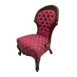 Victorian style mahogany framed nursing chair, the cresting rail carved with fruit and foliage, upholstered in red patterned fabric with buttoned back, on cabriole supports with scrolled terminals