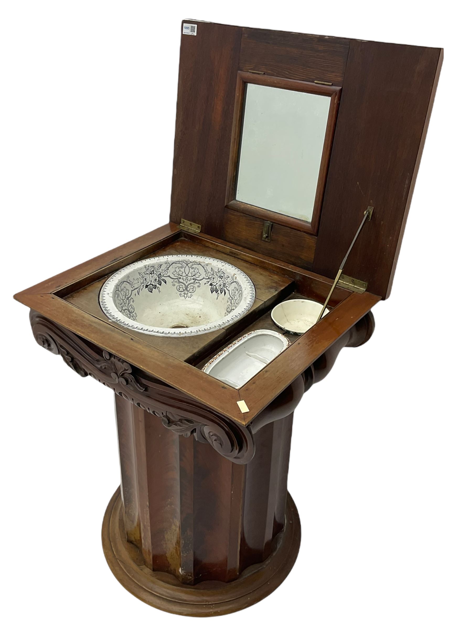 Victorian mahogany vanity unit in the form of a column, the scrolled top with hinged lid revealing mirror, wash bowl and toiletry dishes, on scalloped cylinder pedestal with single door, the interior fitted with shelf