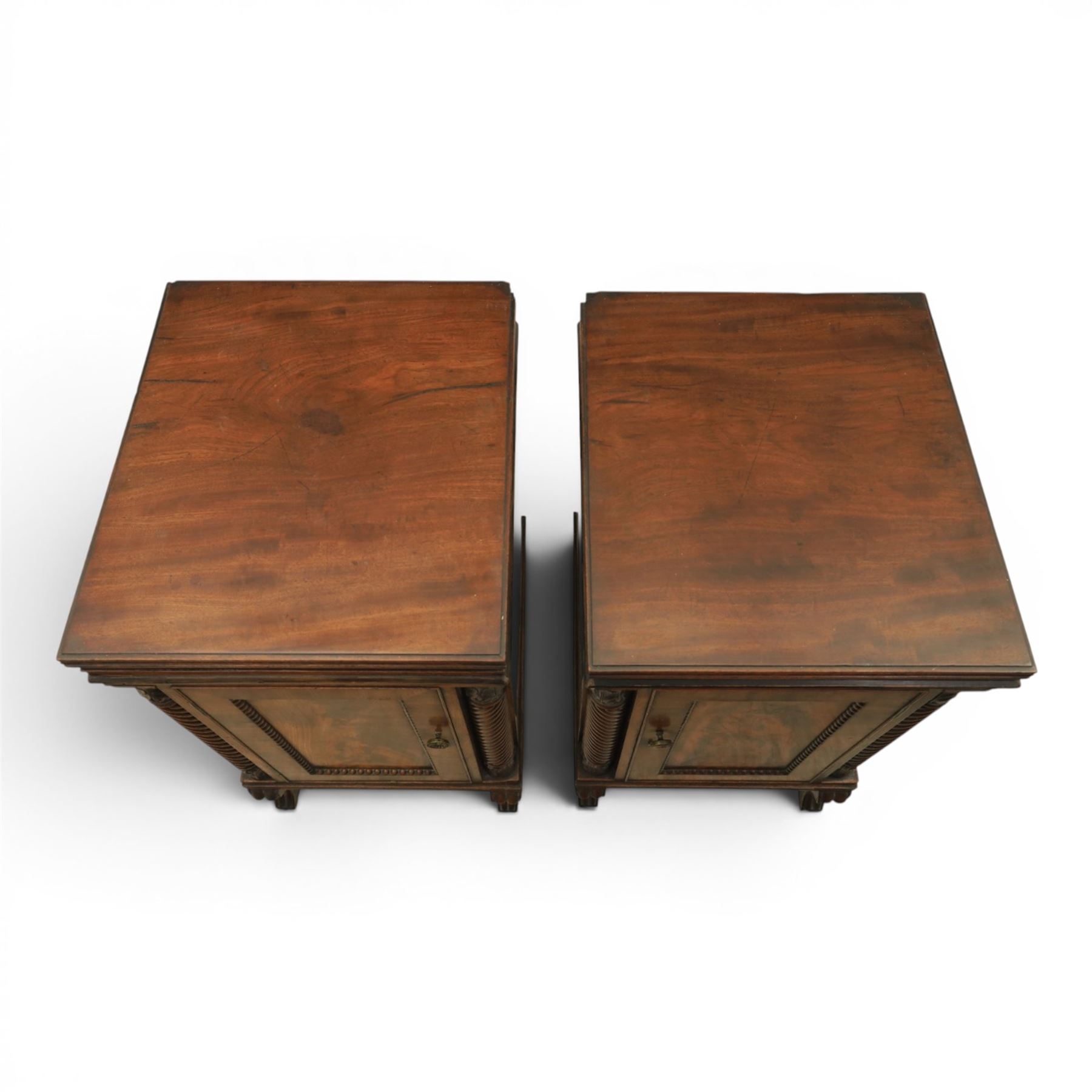  Pair of Regency mahogany bedside cabinets, rectangular top above a central cupboard door with flame mahogany veneer, flanked by spirally turned column uprights, raised on shaped supports