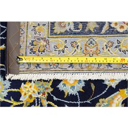 Central Persian Kashan hand-knotted carpet, deep indigo field with a densely all-over arrangement of scrolling floral vines, palmettes, and flowering sprays, in soft ivory, pale blue, and warm gold tones, principal ivory border with a continuous meandering vine of stylized palmettes, and floral motifs, flanked by multiple narrow guard borders, with cotton fringe ends 