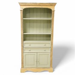 Painted open bookcase over two long drawers and cupboard, with arched cornice above two shelves, in a distressed yellow and sage green 