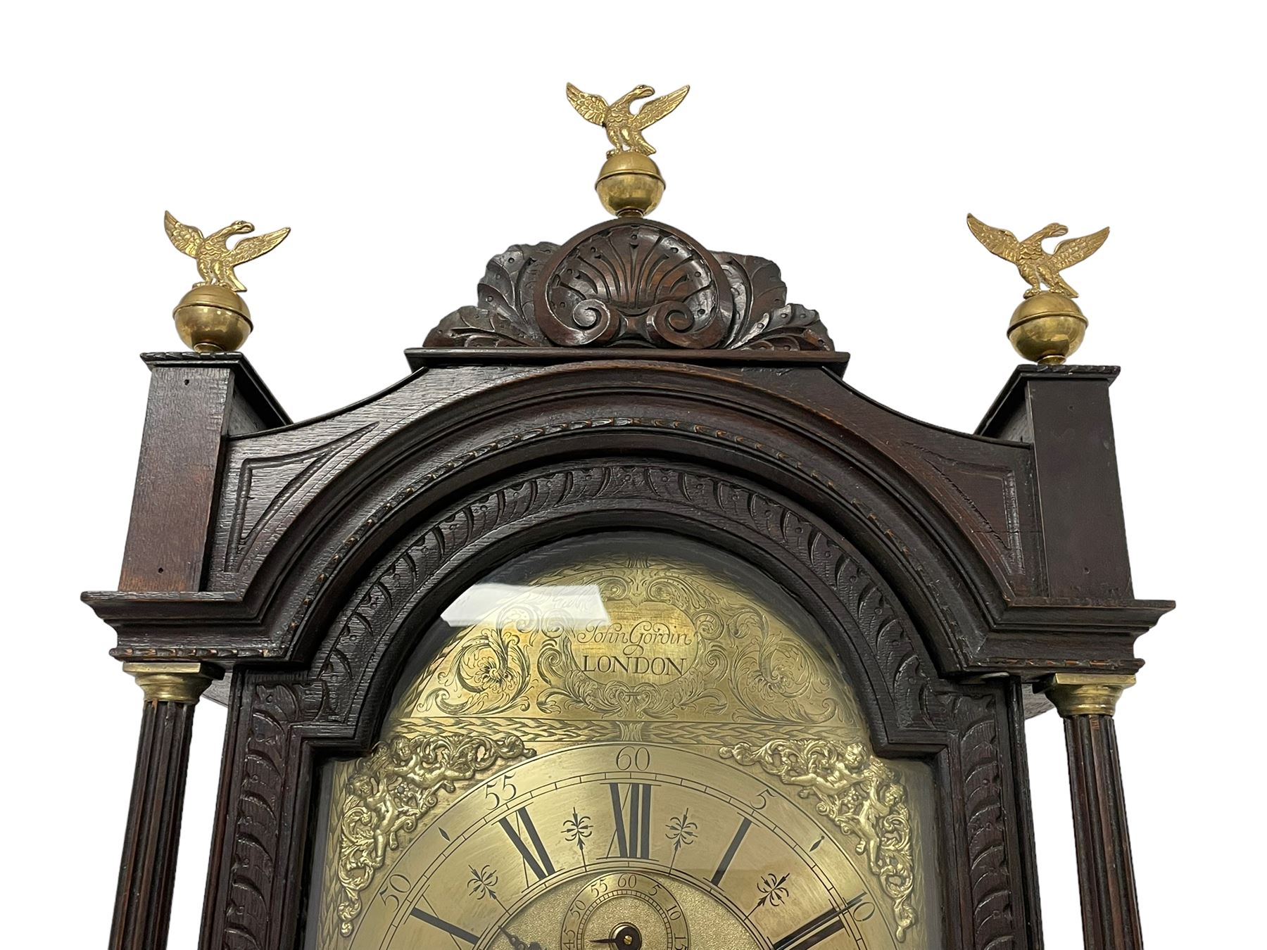 18th-century profusely carved oak longcase clock - with a pagoda pediment, upstands and carving, 
 break arch hood door flanked by reeded pilasters with brass capitals, trunk with canted corners and a spire topped door, square plinth with applied skirting, break arch brass dial with wheatsheaf engraving and cast cherub and crown spandrels, engraved break arch with the London clockmakers name John Gordin, silvered chapter ring with Roman numerals, five minute Arabic's, minute and quarter hour tracks, matted dial centre with ringed winding holes, square date aperture and seconds ring, dial pinned to a five pillar movement with inside countwheel striking, striking the hours on a cast bell. With weights and pendulum. John Gordin, is possibly a mis-spelling or phonetic spelling of John Gordon, of London, who worked from Ludgate Street in the parish of St. Gregory by St. Pauls. Apprenticed in 1689 and died in 1732 when his will was proven.

