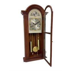 A contemporary Acctim (Anglo continental clock company) thirty-one day striking wall clock in a mahogany effect case with a fully glazed door displaying the pendulum and two dummy wights with chains, with a polished brass dial, Roman numerals, minute track and pierced steel hands, dial plate decorated with spandrels and Tempus Fugit inscribed on the dial brake-arch.
With key and pendulum.


