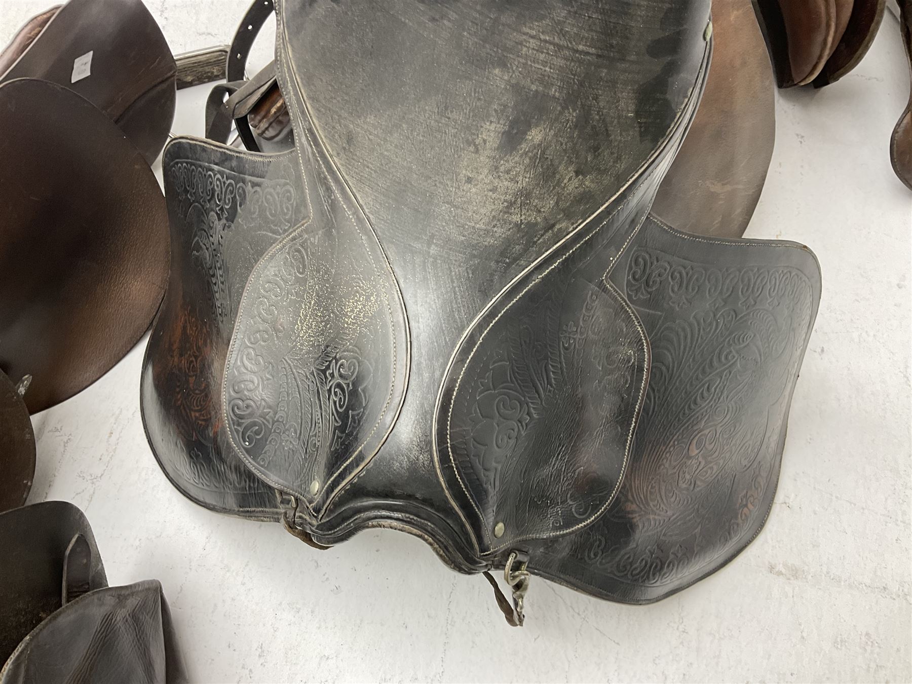 Collection of nine saddles, mainly havana leather to include a racing saddle and a Goodwin saddle, some with stirrups and leathers 