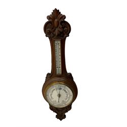 An English 1930’s solid oak carved hall barometer in a scroll shaped carved case with relief carving, aneroid movement, 8” white register measuring barometric air pressure from twenty-six to thirty-one point nine inches, weather predictions in black upper and lower case gothic script with a blue steel indicating hand and brass recording hand, brass dial bezel with flat bevelled glass, mercury thermometer enclosed in a glazed rectangular box displaying temperature in degrees Fahrenheit and Celsius on a white register. H87cm


