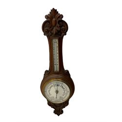 An English 1930’s solid oak carved hall barometer in a scroll shaped carved case with relief carving, aneroid movement, 8” white register measuring barometric air pressure from twenty-six to thirty-one point nine inches, weather predictions in black upper and lower case gothic script with a blue steel indicating hand and brass recording hand, brass dial bezel with flat bevelled glass, mercury thermometer enclosed in a glazed rectangular box displaying temperature in degrees Fahrenheit and Celsius on a white register. H87cm


