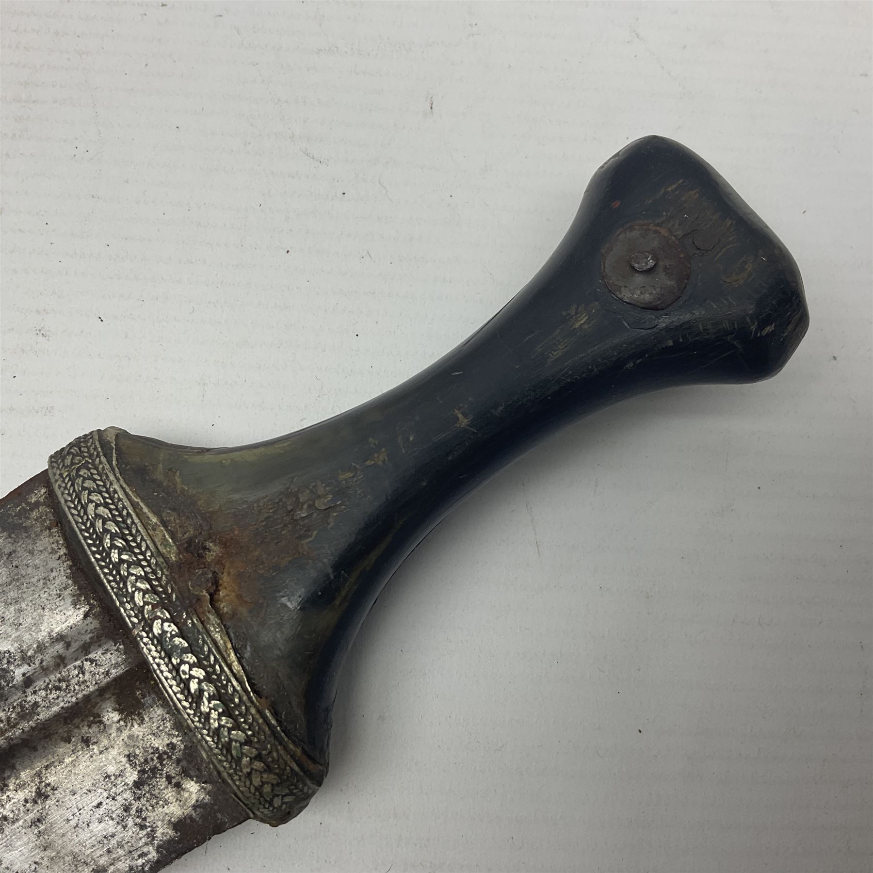 Eastern Jambiya, the 19cm double edge steel blade with raised medial ridge, waisted horn grip with pique work and white metal band; in stitched leather scabbard L33cm overall
