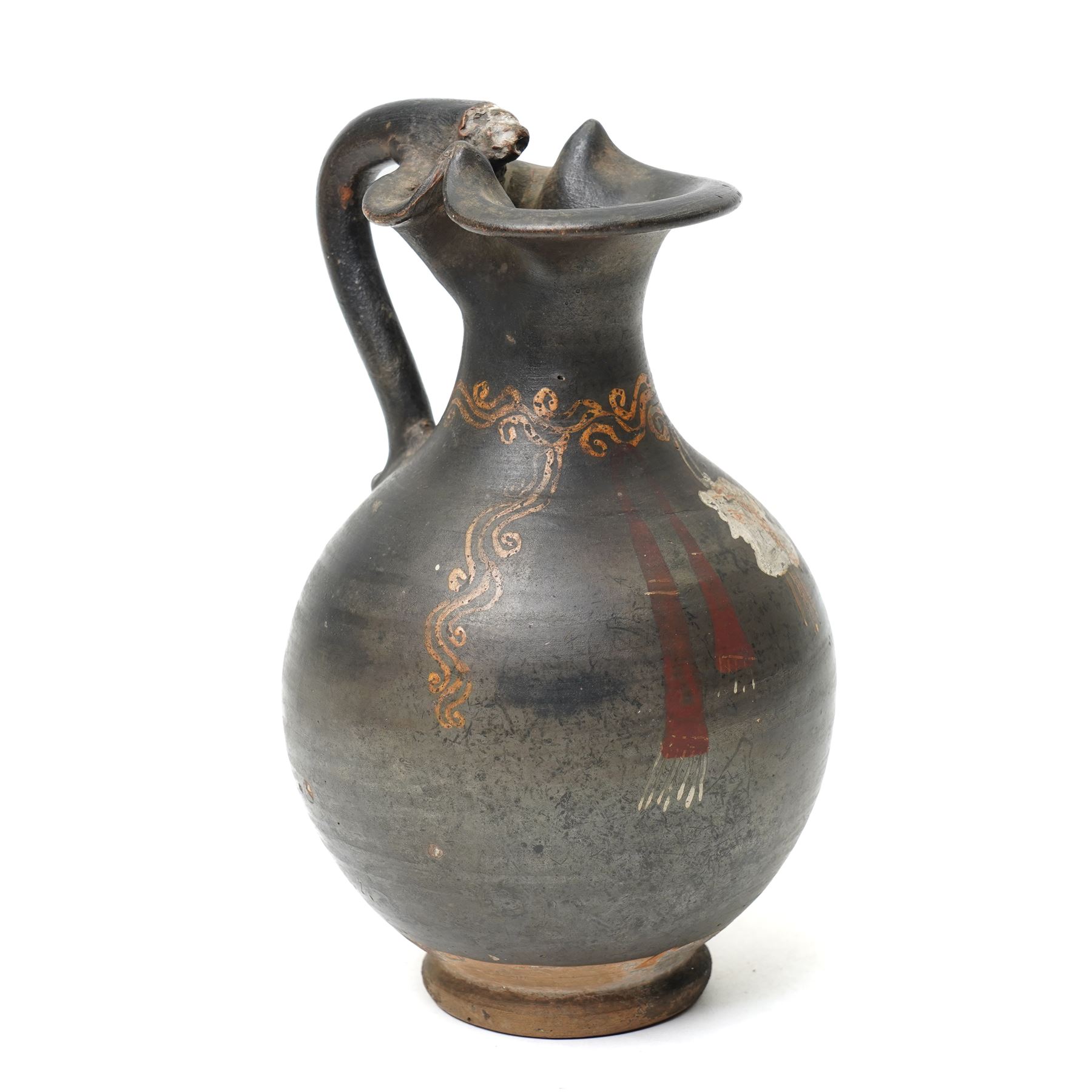 South Italian Gnathian terracotta oinochoe (jug) Apulian or Campanian (Late 4th century BC c.325-300 BC) of elegant ovoid form with trefoil mouth and single strap handle, the handle terminating in a stylised serpentine motif merging into the pouring lip, the vessel covered in a black gloss slip and decorated in added red, white and yellow with a theatrical mask, fillets and scrolling Dionysiac vine motifs, H19cm 
Notes: Gnathian ware takes its name from Egnathia in Apulia and is characterised by a black-gloss ground with added-colour decoration; the theatrical mask, fillets and vine scrolls relate to Dionysiac imagery associated with the symposium and theatre in South Italian Greek culture of the late fourth century BC. A very similar oinochoe is held in the The Metropolitan Museum of Art, object number 76.12.8