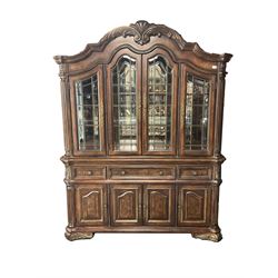 Kevin Charles - American walnut display cabinet, illuminated interior, shell carved pediment above four bevel edge doors enclosing six glazed shelves above one central long drawer flanked by two short drawers, above three cupboards, carved bracket supports 