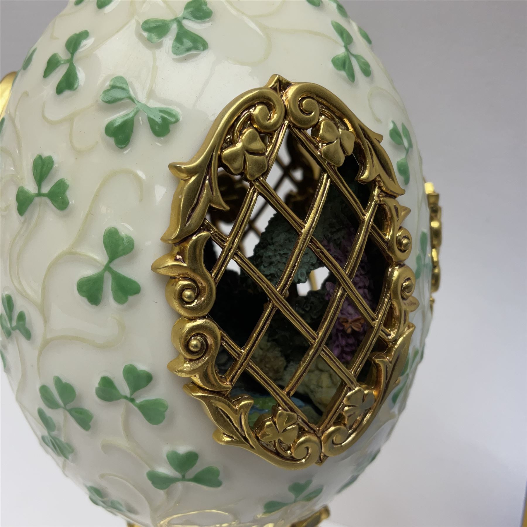 Franklin Mint The Emerald Isle Collector Egg, the egg decorated with embossed shamrocks upon a cream ground, with a gilded shamrock finial, accents and openwork door, opening to reveal a miniature landscape scene, upon three gilded feet set with green paste stones, with certificate of authenticity H23cm, 