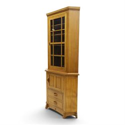 Acorn Industries - oak floor-standing corner cabinet, the top fitted with astragal glazed door enclosing four shaped shelves, the base with single panelled cupboard over two drawers, raised on four stepped feet, carved with acorn signature to top and base, by Alan Grainger, Brandsby