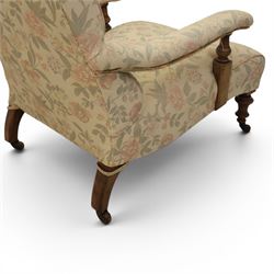 Victorian mahogany framed deep seat low drawing room chair, upholstered in beige floral fabric, on turned supports terminating in castors