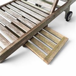 Pair of teak garden sun loungers, with slatted adjustable backrests, integrated wheels and sliding pull-out side trays, weathered natural finish.