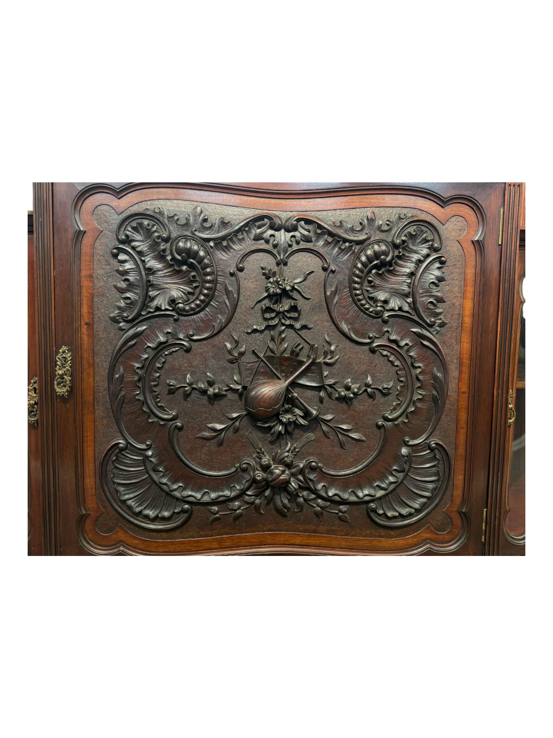 Late 19th century mahogany mirror back cabinet, shaped C-scroll pediment decorated with carved acanthus leaf cartouche and shells, shaped canopy top with applied foliate carvings over triple bevelled mirror back, central cupboard enclosed by panelled door carved with musical instruments, scrolls and shells, flanked by two glazed cabinets, on acanthus leaf carved cabriole supports united by undertier 