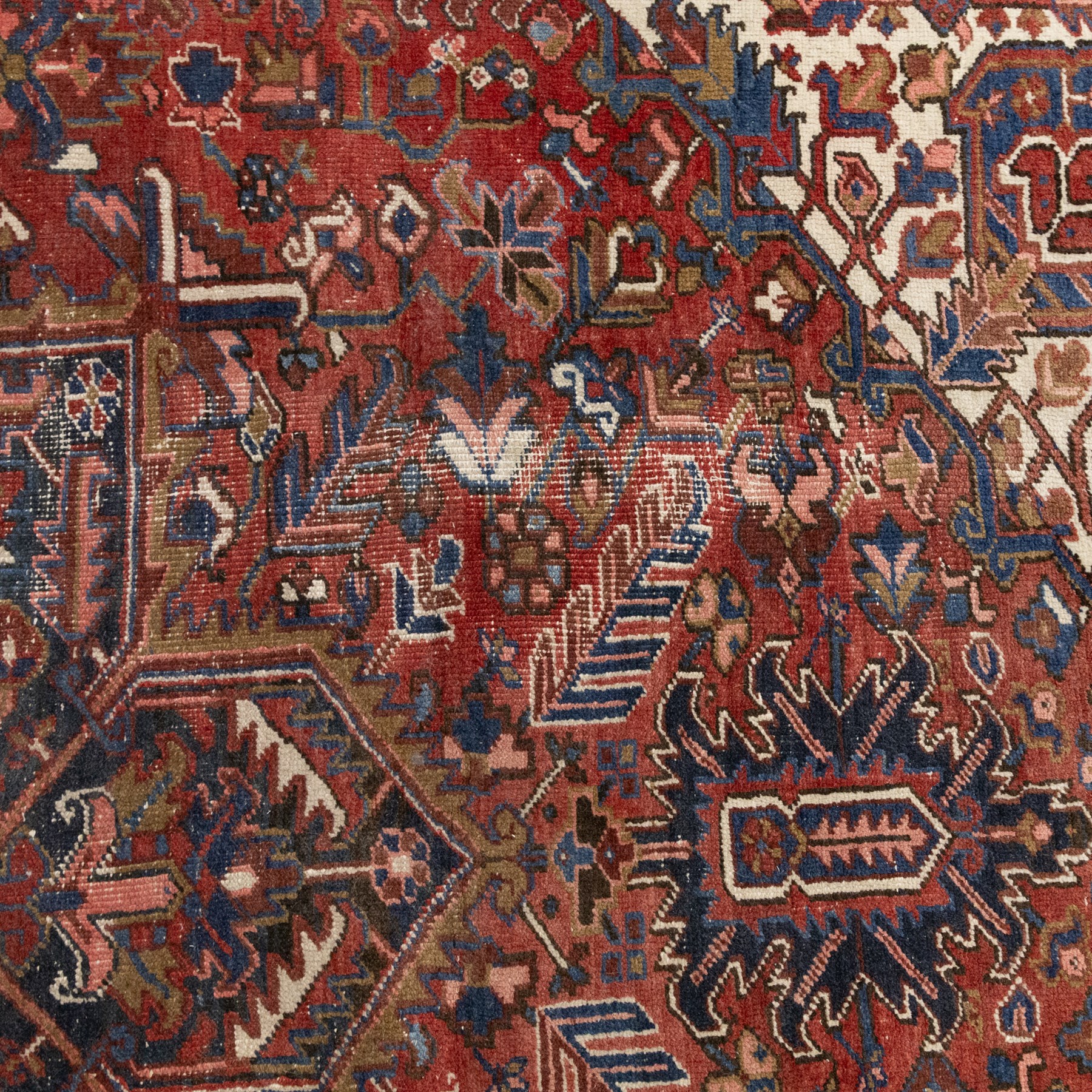Persian Heriz carpet, red ground with large central geometric medallion, angular flowering branches and stylised foliate decoration, within a broad dark blue floral border and narrow guard stripes