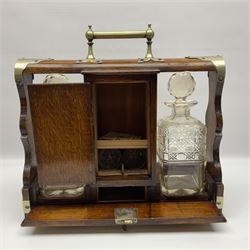 Early 20th century oak tantalus with silver plated mounts and handles, with two recesses, each containing a cut glass decanter, divided by 
a central compartment, the hinged mirrored door opening to reveal two glasses and a shelf, with cribbage board to a drawer below and presentation plaque to body, with key, H36cm W37cm