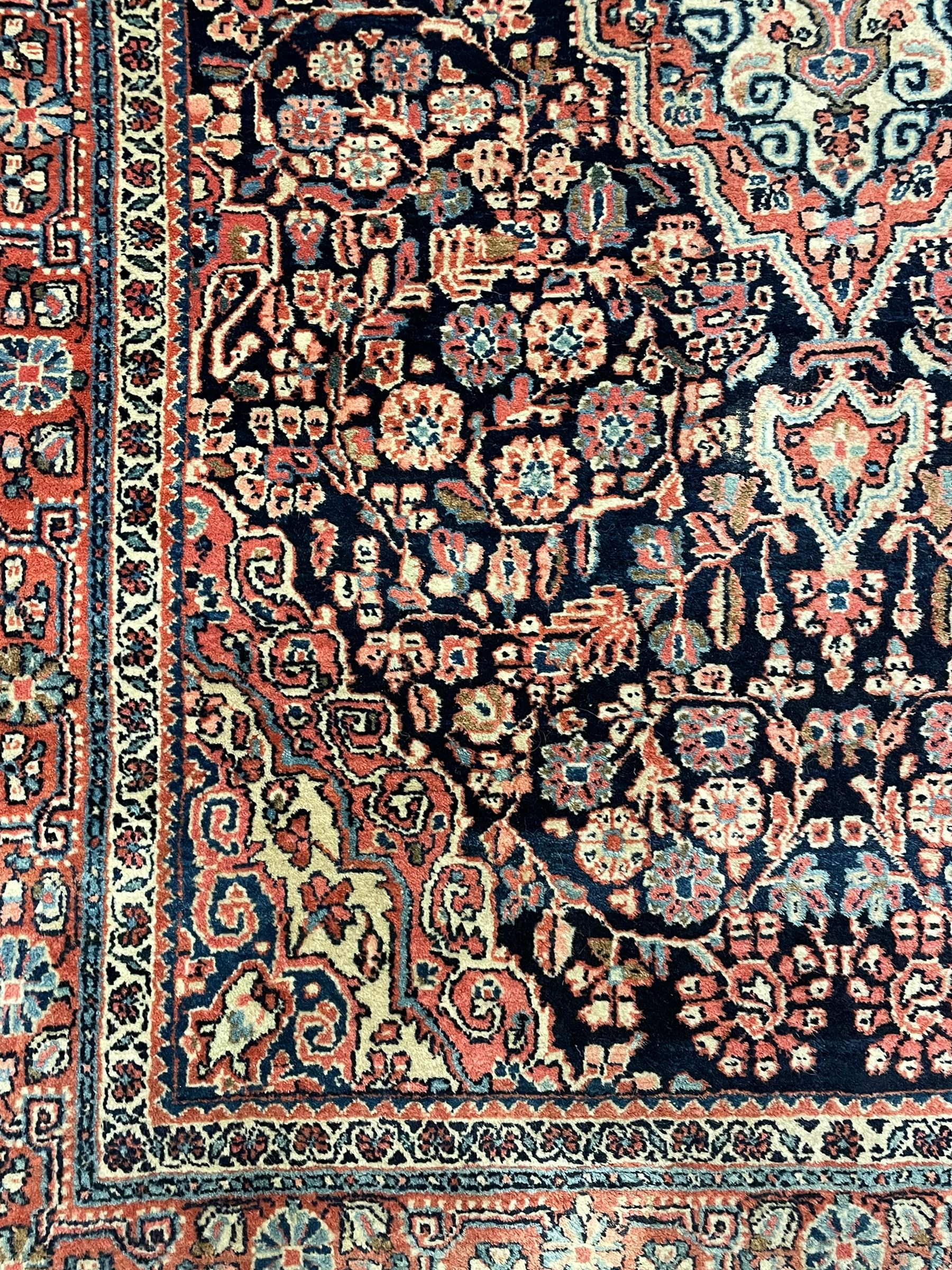 Persian indigo ground rug, the field decorated with intricate interlaced foliage branches and small flower heads, shaped floral design central medallion, the border decorated with scrolling branch and flower heads within guard bands 
