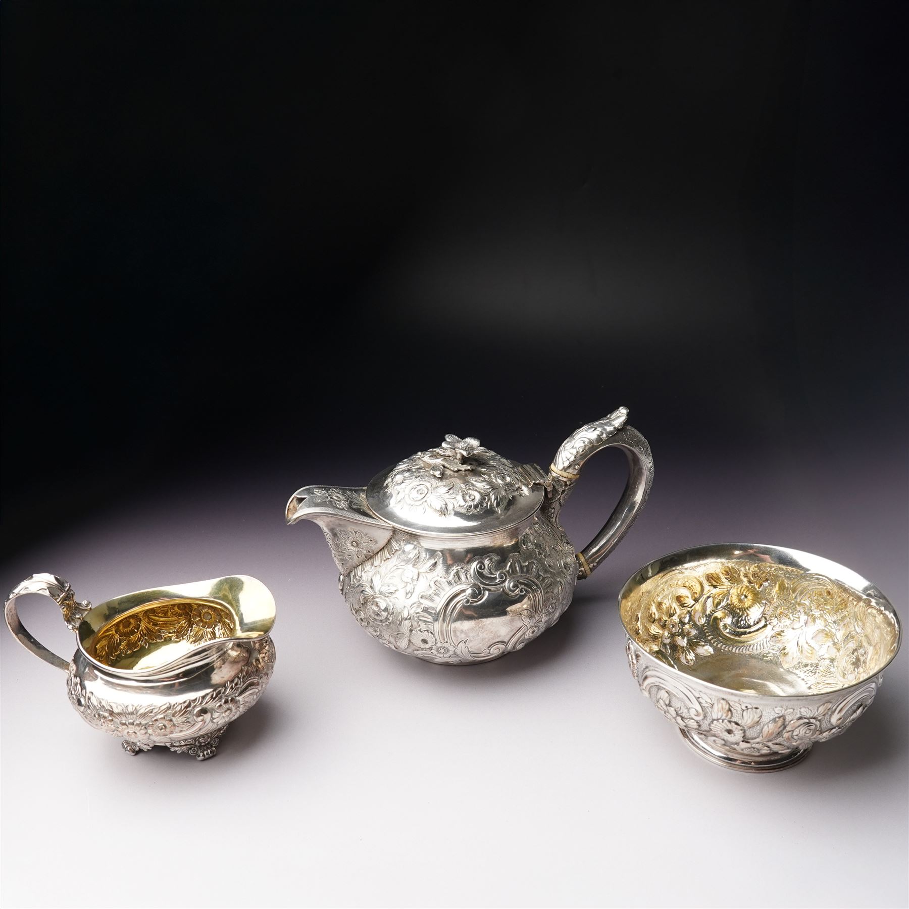 Matched three piece silver tea set comprising teapot of squat circular form London 1827,  milk jug of similar date and sugar bowl with Britannia standard marks, all with later embossed floral decoration and coat of arms, all marks rubbed